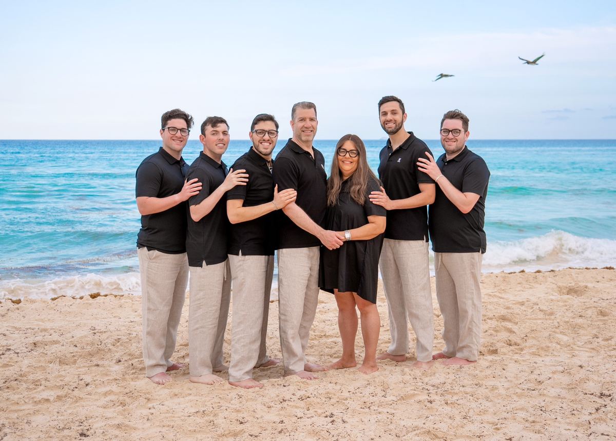 Lara Goulson with her husband and five sons, all in matching black shirts, standing barefoot on the beach by the ocean